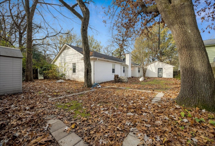 View of property exterior featuring brick siding, a chimney, a storage shed, and a shingled roof
