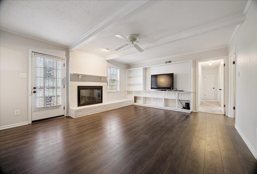 Unfurnished living room featuring beamed ceiling, a textured ceiling, dark wood finished floors, ceiling fan, and ornamental molding