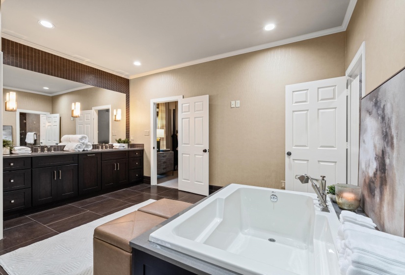 Built-in soaking tub with brushed nickel fixtures, complemented by dark wood-finish cabinetry, a full-width vanity mirror, and recessed ceiling lighting