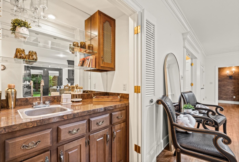 Wet bar featuring a stainless steel sink, brown patterned countertop, and wood-finish cabinetry