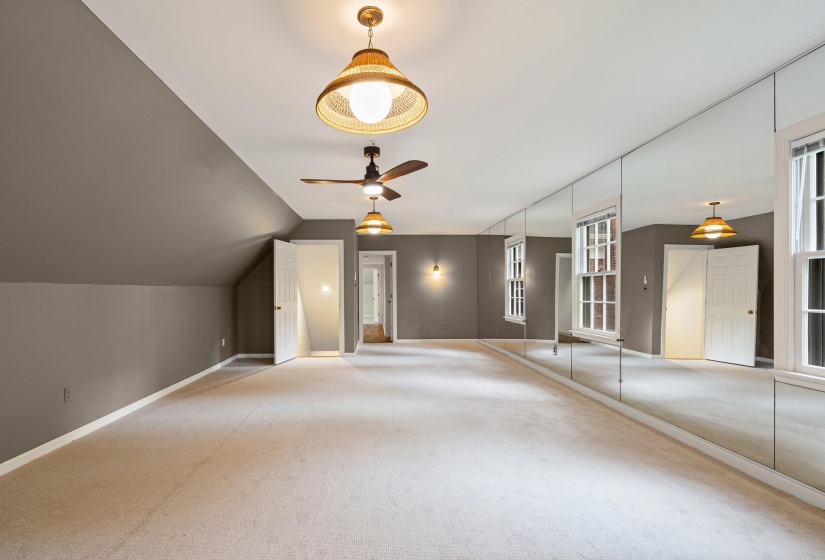Spacious room featuring a full mirrored wall, two windows, two ceiling fans with integrated lighting, and two additional ceiling-mounted light fixtures