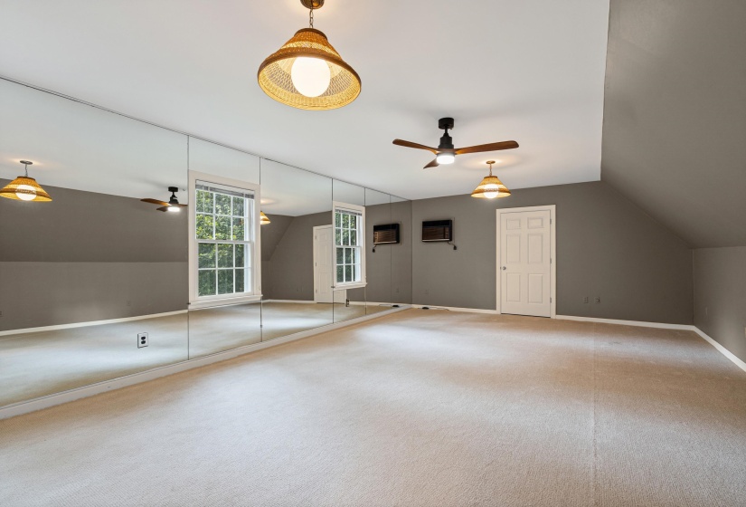Spacious bonus room featuring wall-to-wall carpeting, multiple windows, a ceiling fan, and built-in wall mirrors