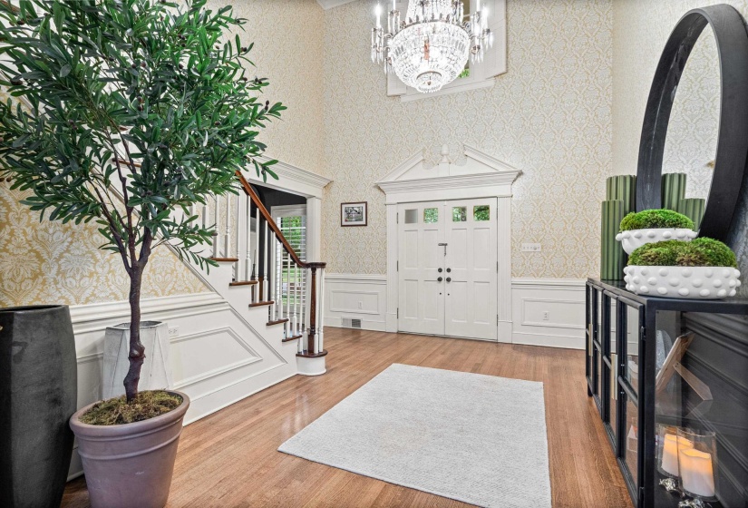 Two-story foyer featuring hardwood flooring, an elegant chandelier, wainscoting, and a grand staircase with wood banister