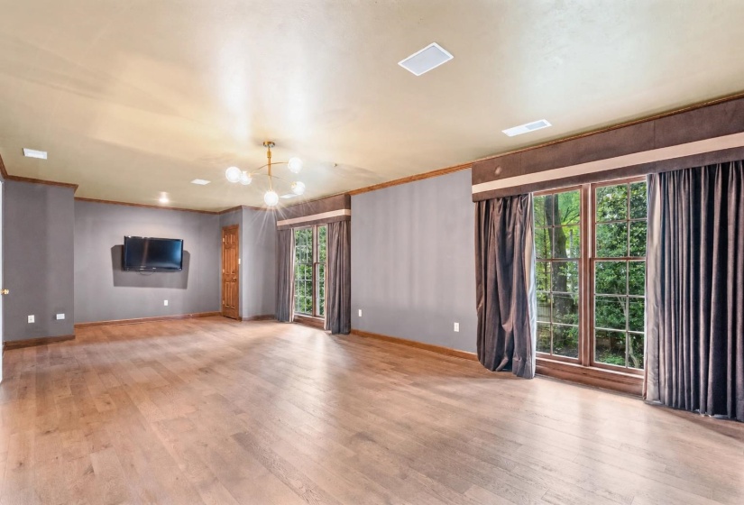 Spacious room featuring wood-finish flooring, a contemporary chandelier, recessed ceiling lighting, and large windows with exterior foliage