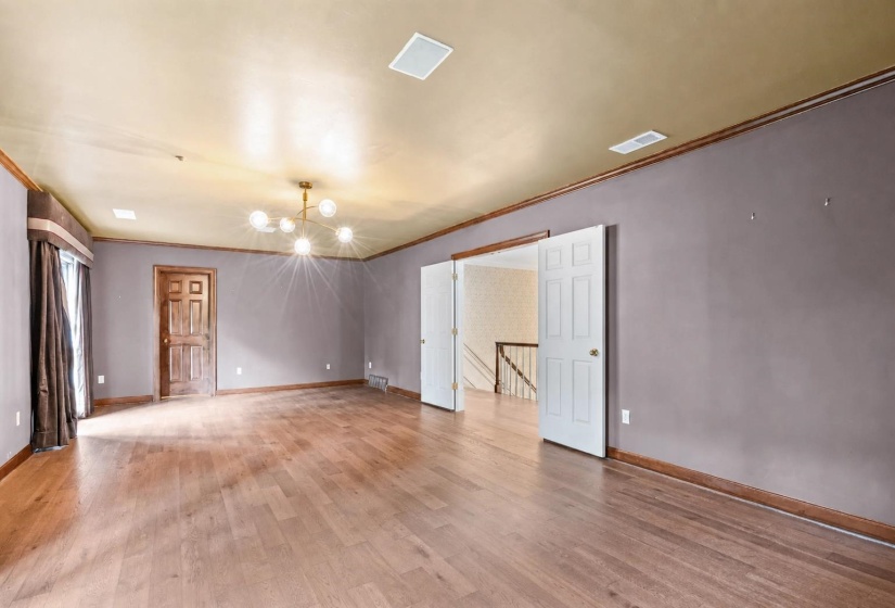 Spacious interior room featuring wood-finish flooring, a contemporary chandelier, two panel doors, and a window with drapery