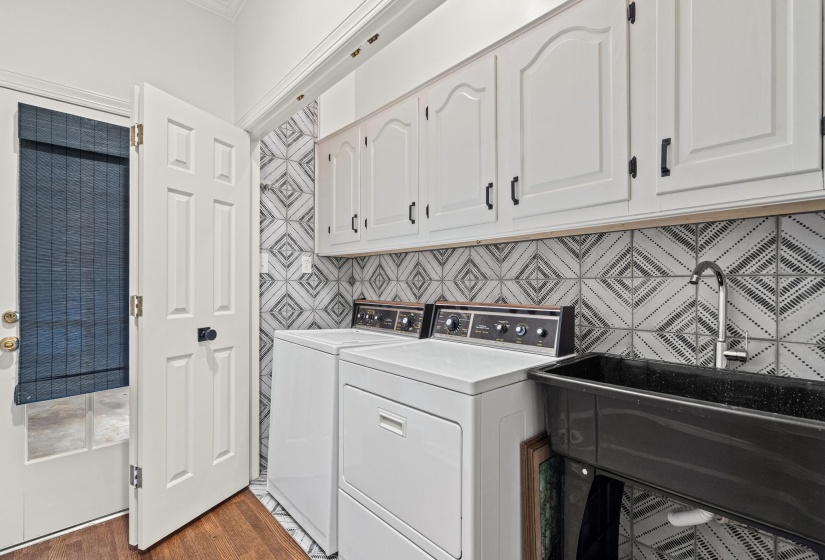 Functional utility space featuring wood-finish flooring, white paneled cabinetry with black hardware, and patterned wall tile