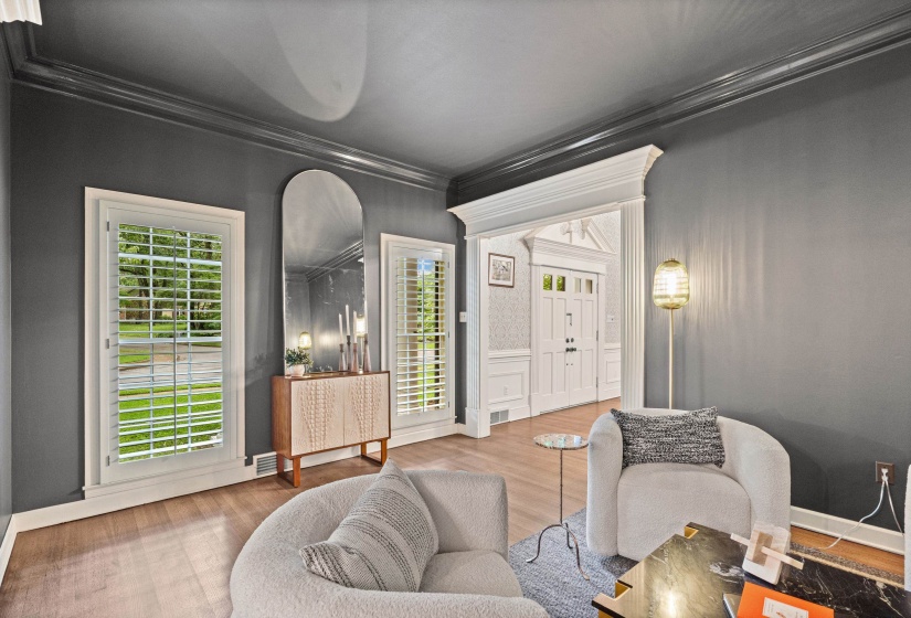 Living area featuring hardwood-finish flooring, plantation shutters, crown molding, and a decorative archway