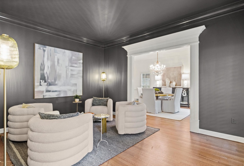 Open concept living area with dark gray walls, crown molding, wood-finish flooring, and a wide cased opening featuring fluted columns
