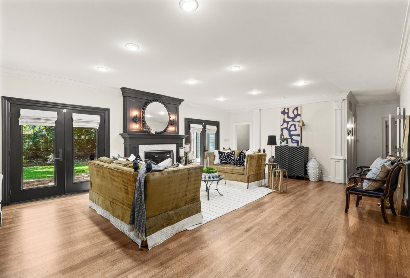 Spacious living area featuring wood-finish flooring, recessed lighting, and a prominent fireplace with a dark mantel