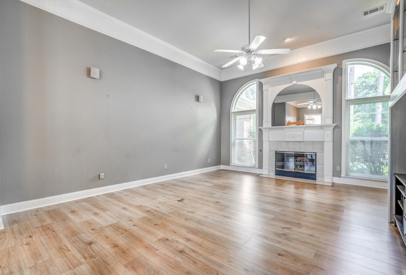 Spacious living area featuring wood-finish flooring, a white mantel fireplace with a dark tile surround, and two arched windows