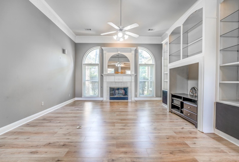 Spacious living area featuring wood-finish flooring, a ceiling fan, and crown molding