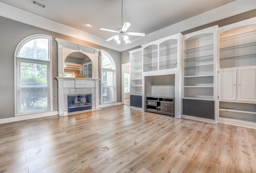 Spacious living area featuring wood-finish flooring, a ceiling fan, and crown molding