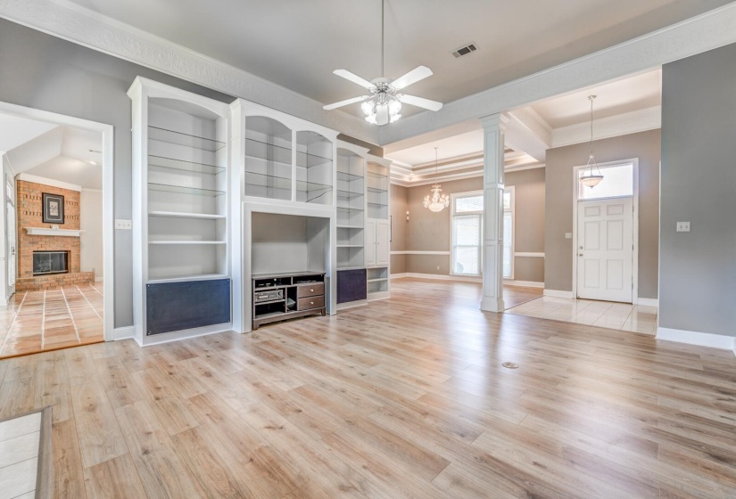 Spacious living area featuring light wood-finish flooring, built-in shelving, a ceiling fan, and a wide entryway with columns