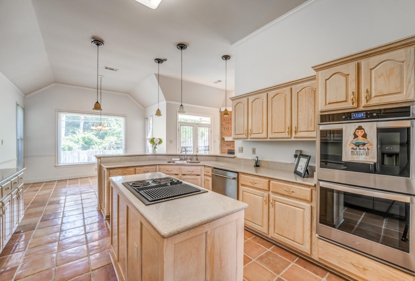 Kitchen featuring an island cooktop, double wall ovens, wood cabinetry, stainless steel dishwasher, and terracotta tile flooring