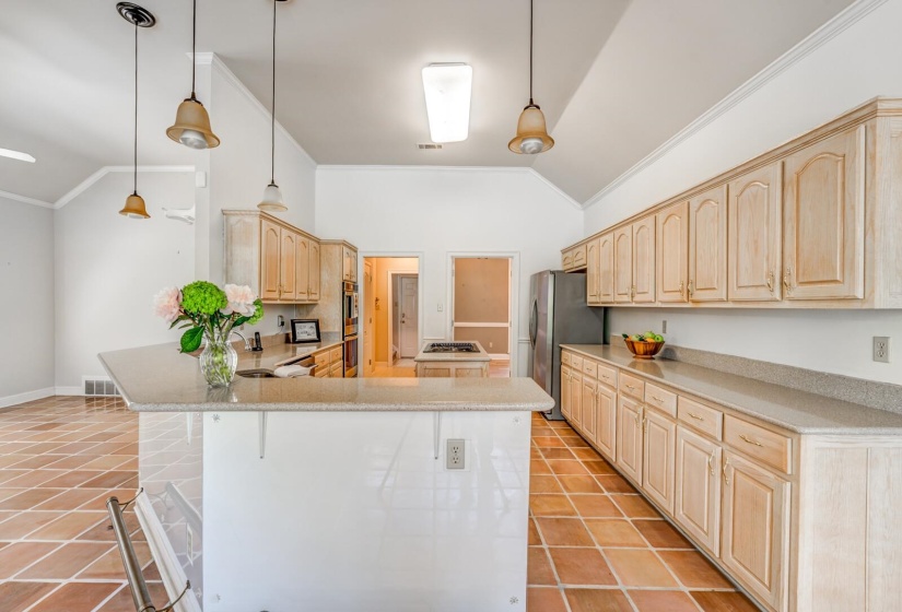Spacious kitchen featuring light wood cabinetry, light-toned countertops, a central island with a breakfast bar, stainless steel appliances, and terra cotta tile flooring