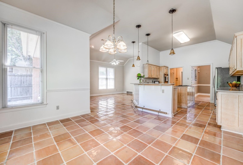 Open-concept living space featuring terracotta tile flooring, vaulted ceilings, and a kitchen island with pendant lighting