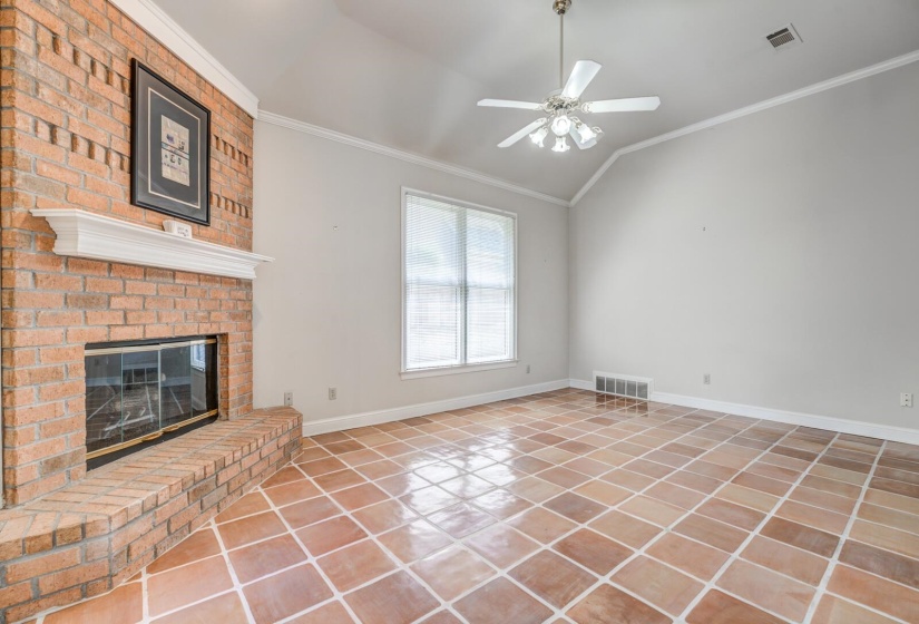 Living area featuring a brick fireplace with a white mantel, large window, vaulted ceiling, ceiling fan, and ceramic tile flooring