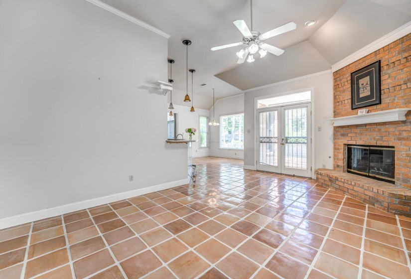 Spacious living area featuring terra cotta tile flooring, a brick gas fireplace with a white mantel, vaulted ceilings, and a ceiling fan