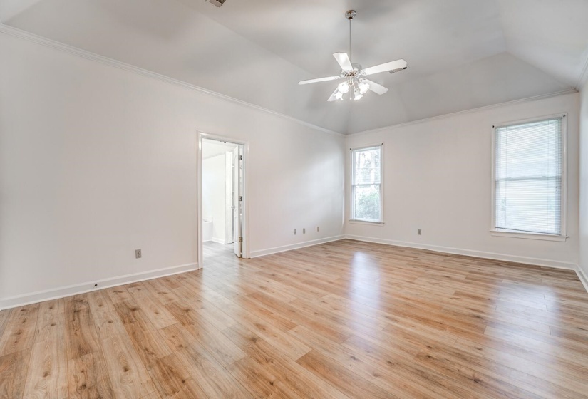 Spacious room featuring vaulted ceilings, wood-finish flooring, and crown molding
