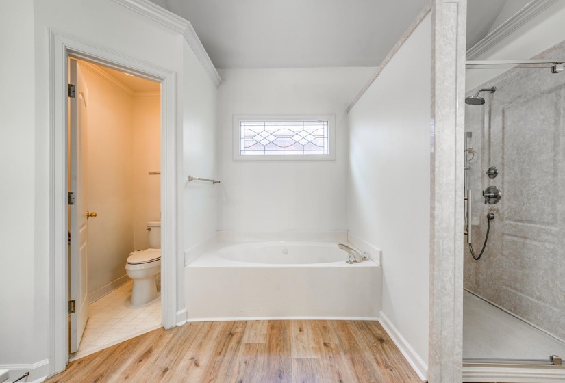 Bathroom featuring a soaking tub with decorative window, separate glass-enclosed shower with multiple sprayers, wood-finish flooring, and crown molding