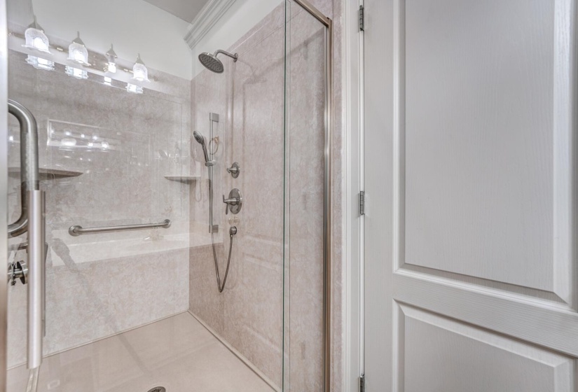 Walk-in shower featuring a glass enclosure, multiple showerheads, integrated seating, and grab bars