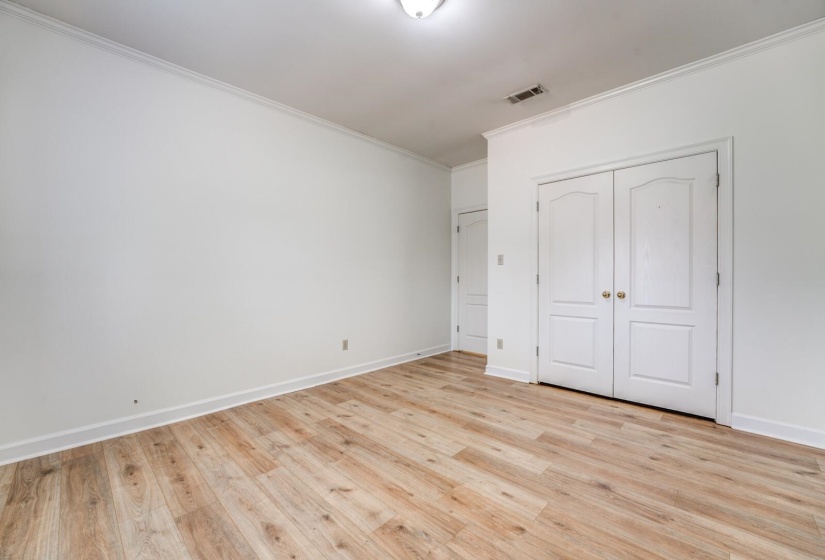Spacious room featuring wood-finish flooring, white walls, and elegant crown molding