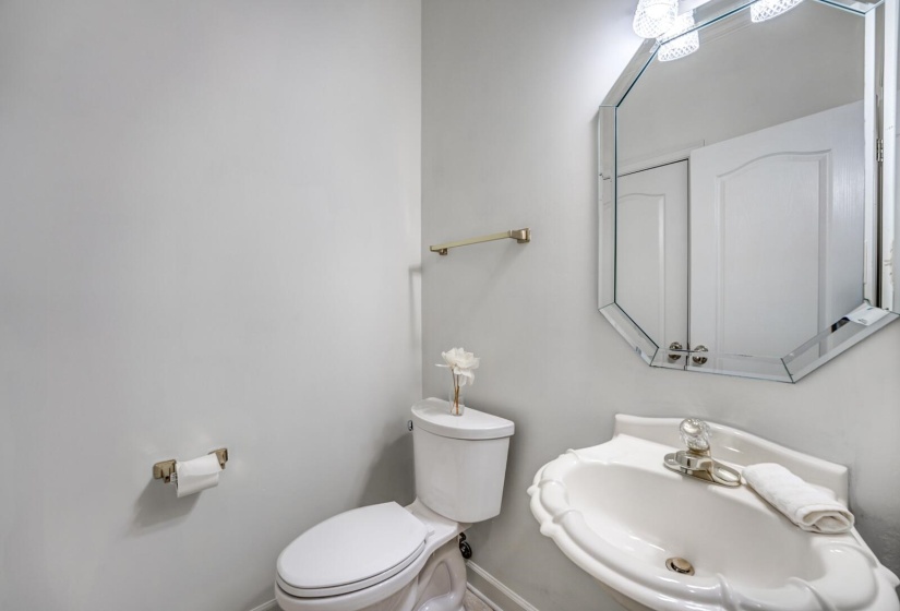 Powder room featuring a pedestal sink with decorative trim, an octagonal mirror, and a two-bulb vanity light fixture