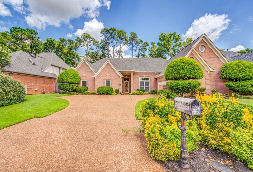 Brick facade residence featuring a gravel driveway, mature perimeter trees, and manicured landscaping with flowering shrubs