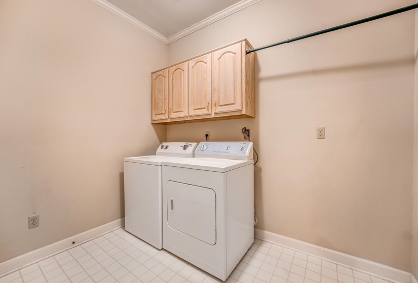 Dedicated laundry area featuring light wood cabinetry, crown molding, a built-in hanging rod, and light-toned floor tiles