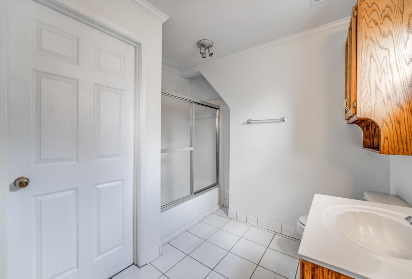 Bathroom featuring a shower-tub combination with sliding glass doors, a single vanity with a laminate countertop, and wood-finish cabinetry