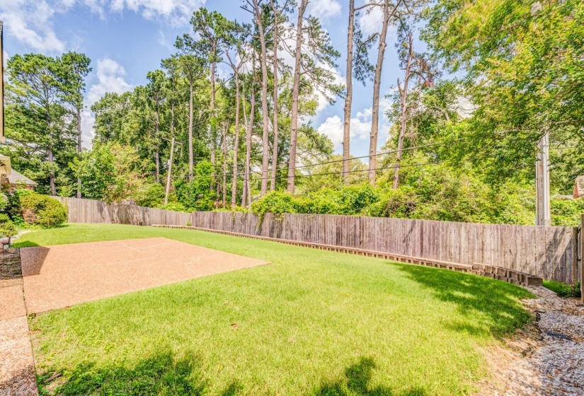 Spacious backyard featuring a large concrete patio, manicured lawn, and a privacy fence
