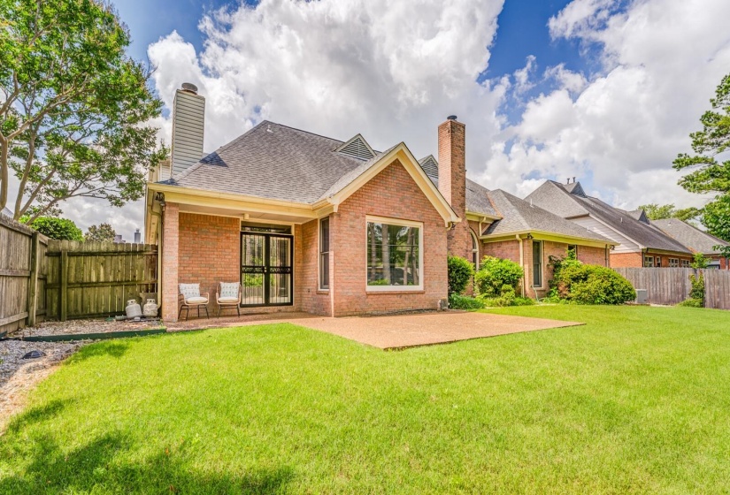Expansive rear lawn featuring a brick exterior, covered patio, and a paver patio