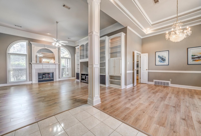 Spacious interior featuring wood-finish flooring, a decorative fireplace with a mantel, built-in shelving, arched windows, and a coffered ceiling with a chandelier