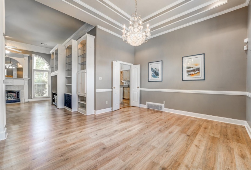 Spacious interior featuring wood-finish flooring, a tiered tray ceiling with a chandelier, and built-in shelving
