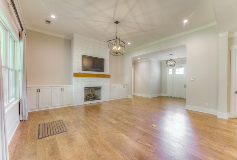 Open-concept interior featuring wood-finish flooring, a white brick fireplace with a wood mantle, and built-in white cabinetry