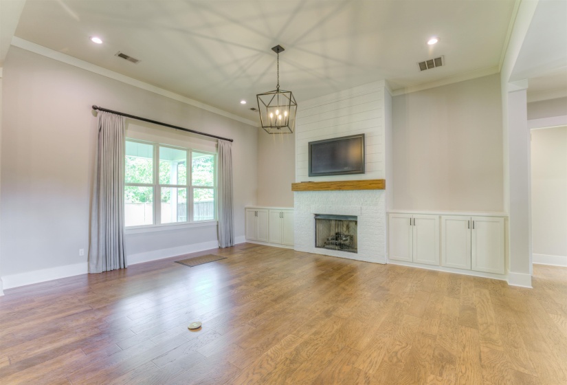 Spacious living area featuring wood-finish flooring, a white painted brick fireplace with a wood mantel, and built-in cabinetry