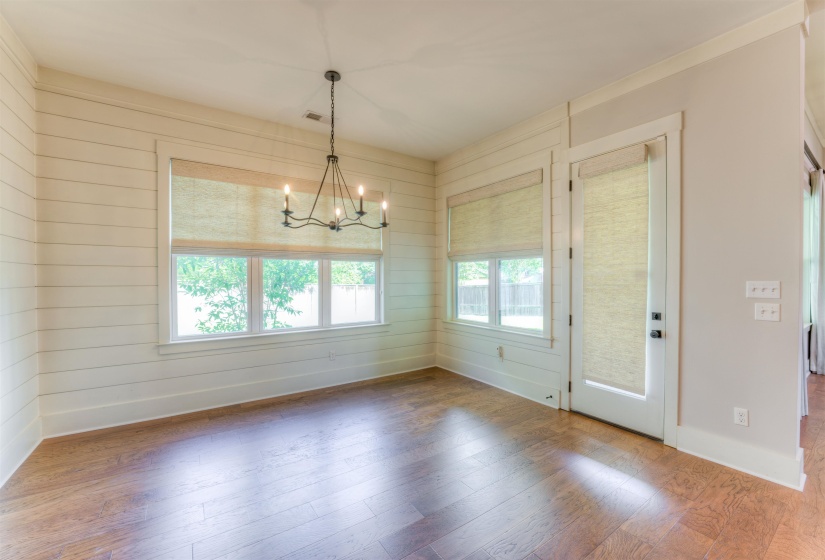 Room featuring wood-finish flooring, shiplap accent wall, multiple windows with blinds, a glass-paned door, and a chandelier