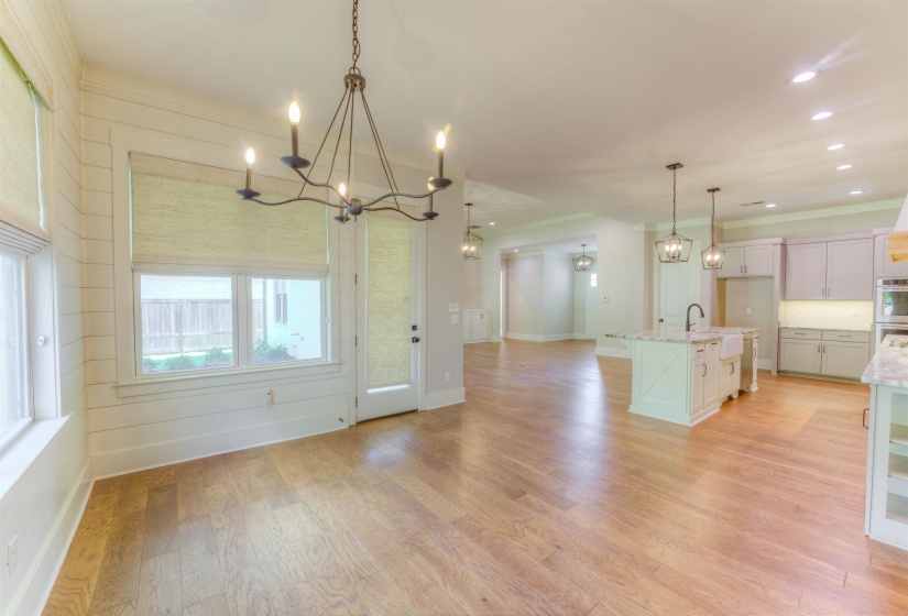Open-concept living space featuring wood-finish flooring, a kitchen island with a farmhouse sink, light-toned cabinetry, recessed lighting, and a modern chandelier