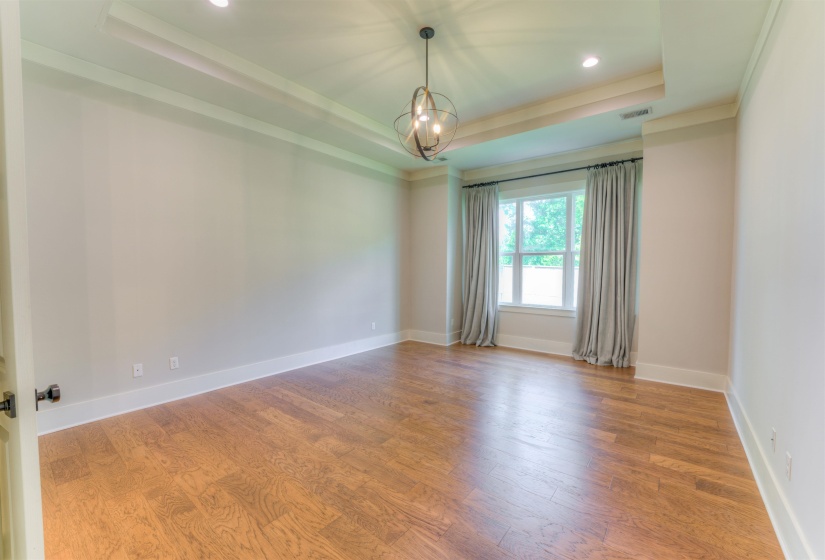 Hardwood flooring extending throughout, tray ceiling with recessed lighting, and a contemporary chandelier