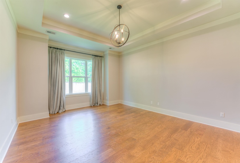 Hardwood flooring paired with a tray ceiling featuring a contemporary chandelier