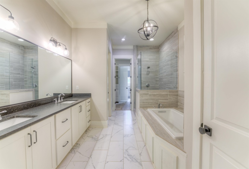 Spacious bathroom featuring a double vanity with stone countertops, a large soaking tub, a walk-in shower with tile surround, and marble-look tile flooring