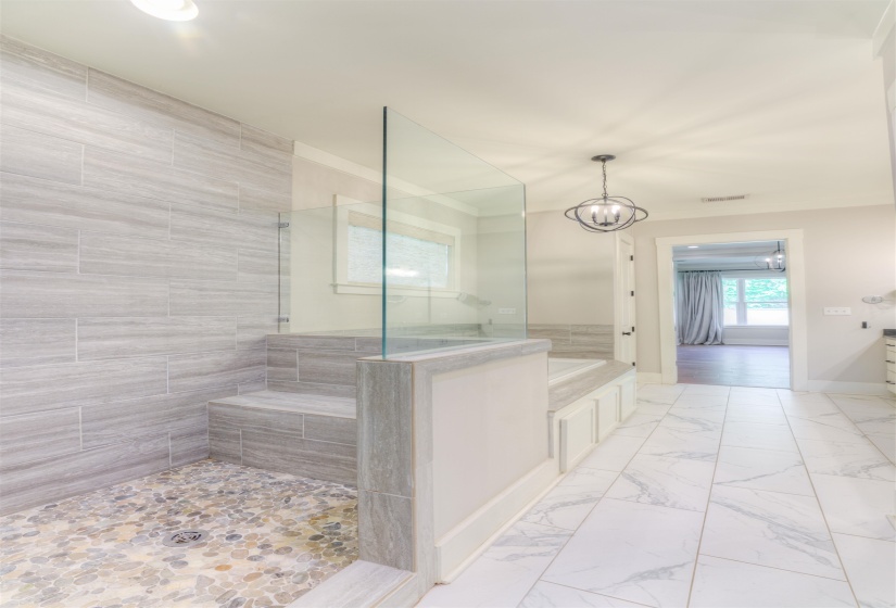 Spacious bathroom featuring a pebble-tiled walk-in shower with a built-in bench, clear glass enclosure, and light gray stone-look wall tiles