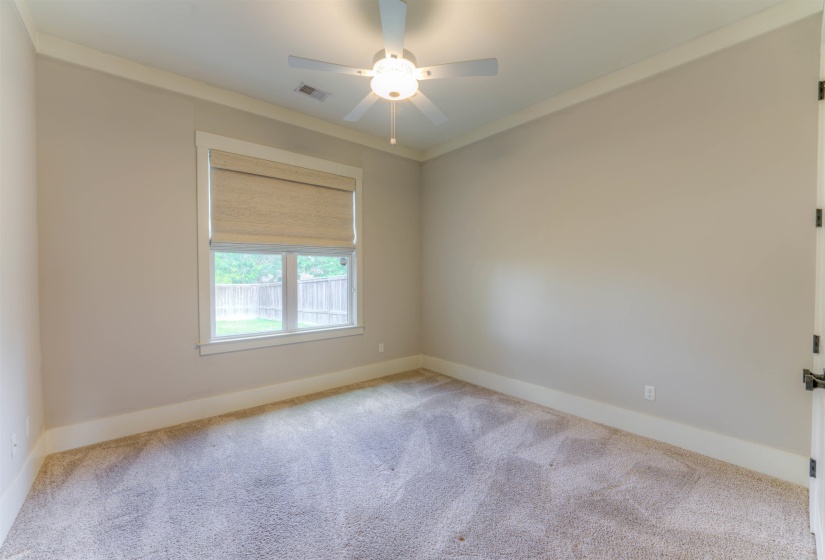 Carpeted room featuring a window with a neutral-toned shade, a ceiling fan with integrated lighting, crown molding, and a white baseboard