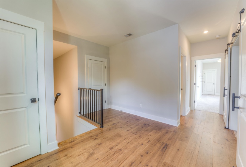 Upper-level hallway featuring wood-finish flooring, white trim, recessed lighting, and a black metal stair railing