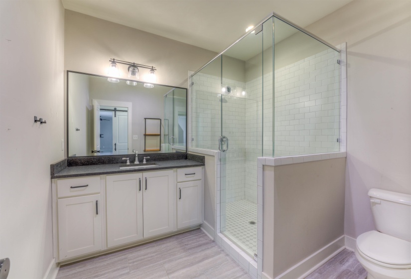 Modern bathroom featuring a glass-enclosed shower with subway tile, an extended vanity with a dark countertop, white shaker-style cabinetry, and wood-finish flooring