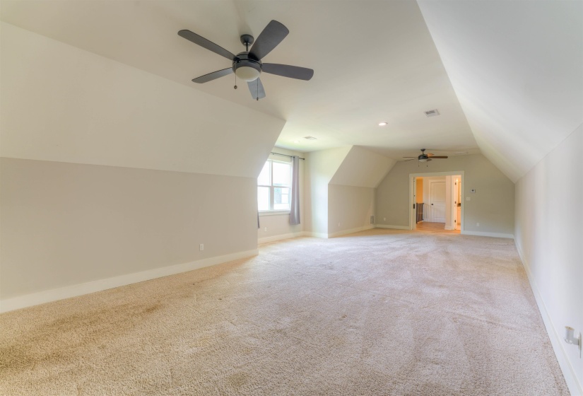 Spacious carpeted room featuring vaulted ceilings, a window, two ceiling fans with integrated lighting, and multiple doorways