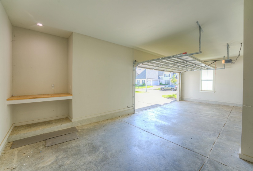 Spacious garage featuring a concrete floor, built-in workbench with storage, recessed lighting, and an overhead garage door mechanism