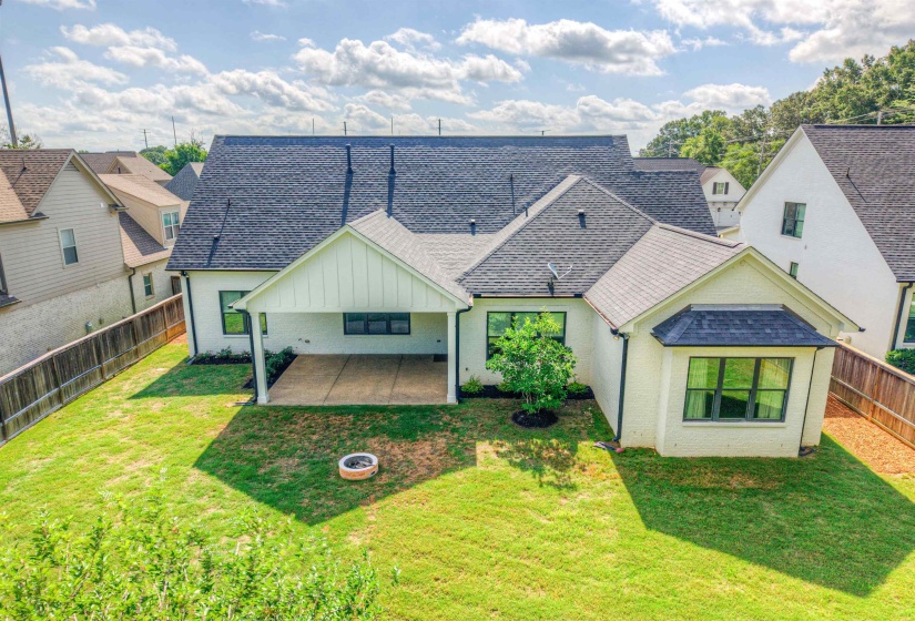 Rear exterior featuring a covered patio with concrete flooring, a bay window with dark trim, and a manicured lawn