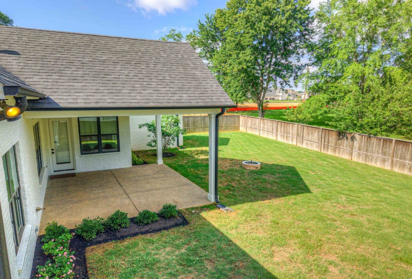 Expansive backyard featuring a covered patio, a fire pit, a wood privacy fence, and mature trees