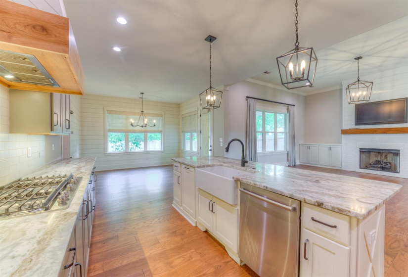 Open-concept kitchen featuring an island with an undermount farmhouse sink, light-toned countertops, white cabinetry, and stainless steel appliances